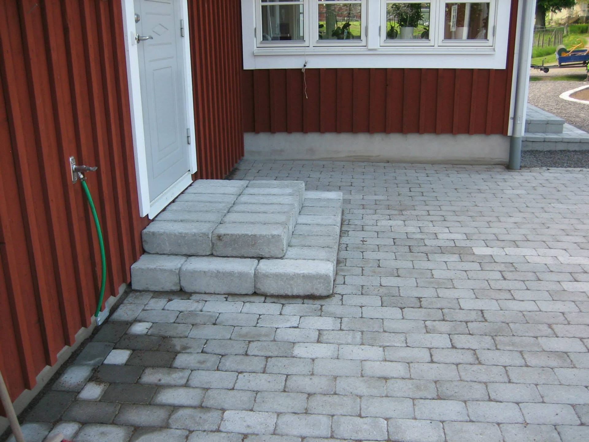 Stenlagd patio med blocktrappa upp till röd fasad