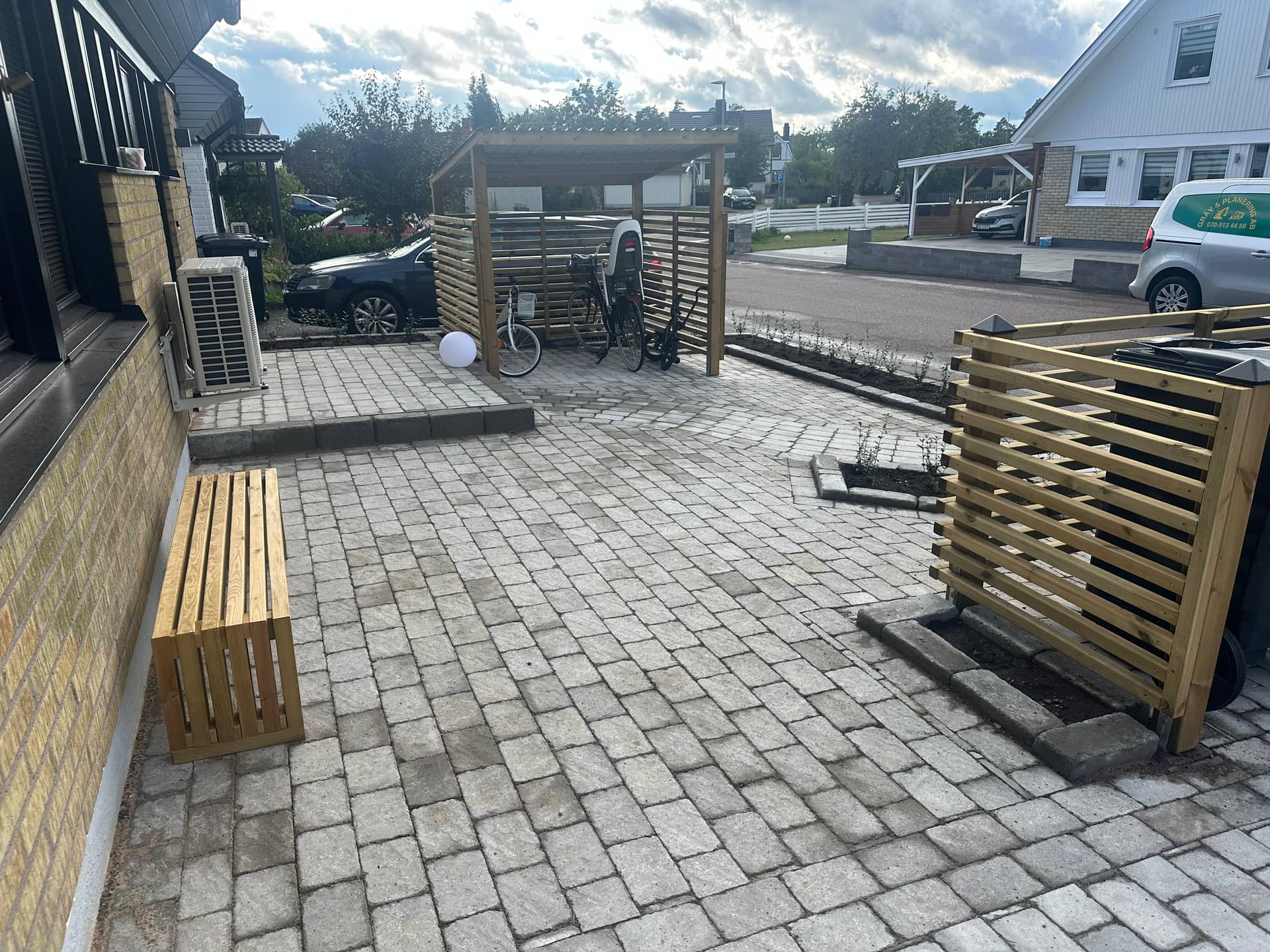 Cykelskjul och soptunnor på nylagd plattläggning vid gult tegelhus