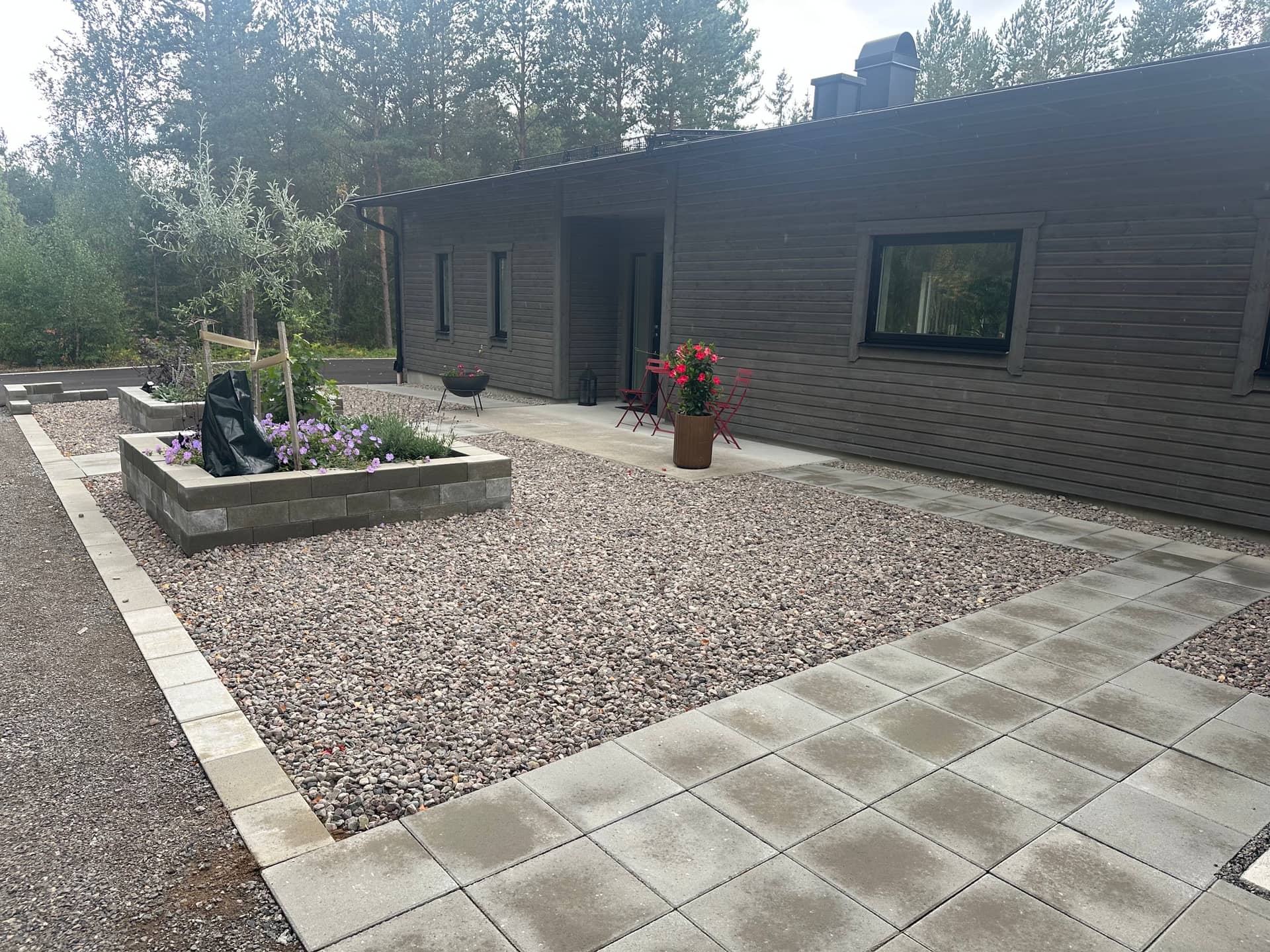 Plattlagda gångar, grusytor och upphöjda rabatter mot mörkt trähus