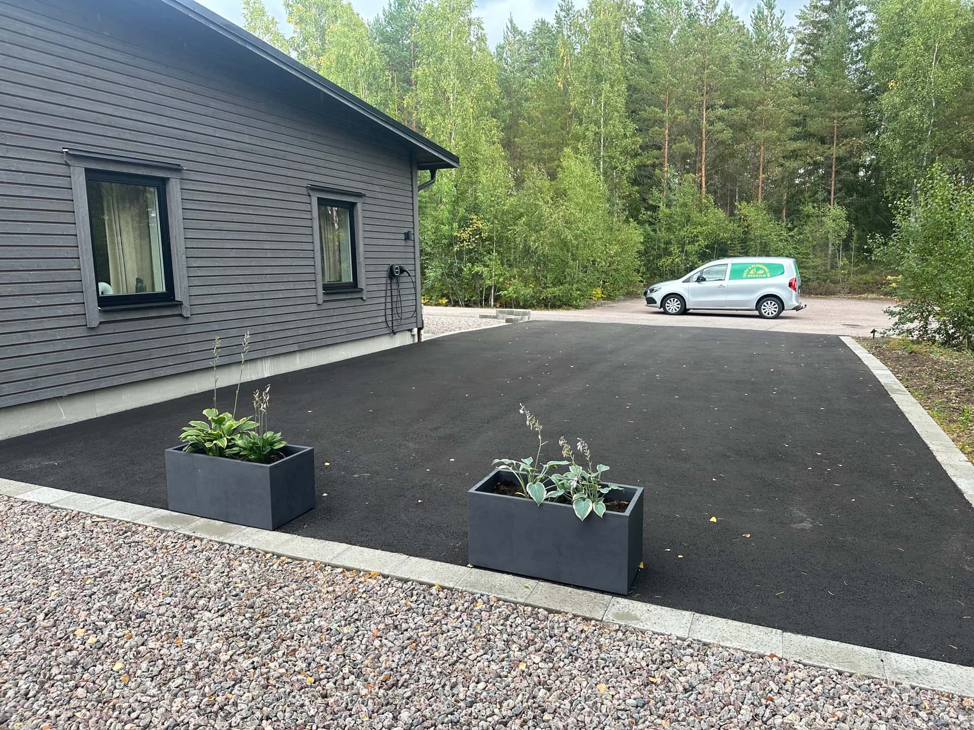 Asfalterad uppfart med kantsten och grusyta mot husfasad