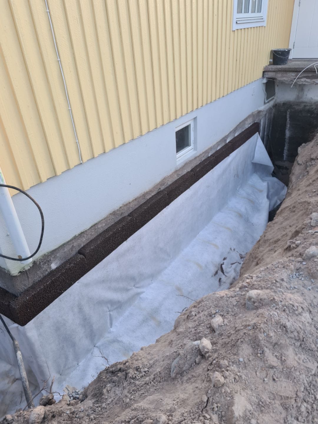 Schakt längs husgrund med geotextilduk och dräneringsplatta mot grunden